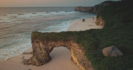 Indonesia landmark closeup aerial: giant hole on cliff wall of Batu Bolong, Bawana Beach, Sumba Island. Unique geological formation with green grass and building on top. Summer nobody nature landscapeの写真素材