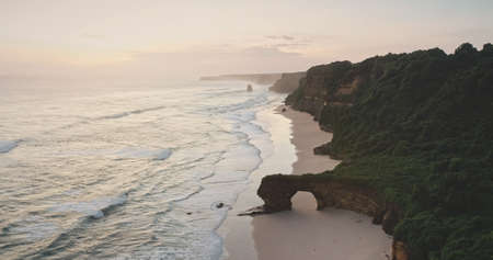 Sunrise at ocean cliff shore with giant hole at rock wall aerial view. Tropical nature landscape of paradise sand beach and green grass rocky coast. Tourist attraction of Sumba Islandの写真素材
