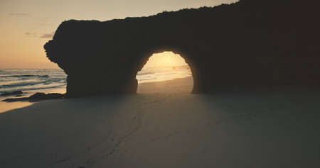 Rock wall, giant hole at sun silhouette aerial view. Sand ocean coast tourist landmark at Bawana Beach, Sumba Island, Indonesia. Summer morning attraction of tropic paradise at sunlightの写真素材