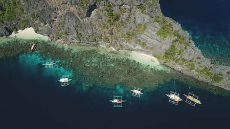 Boats at cliff ocean shore with sand beach at coast aerial view. Nature beauty of tropic mountainous islet in top down drone shot. Amazing seascape with vessels at rock shoreline. Cinematic soft lightの写真素材