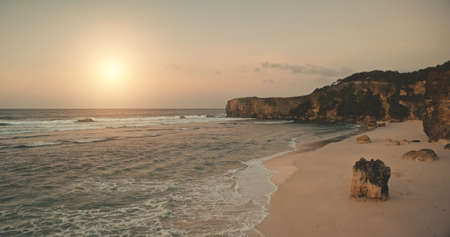 Sand beach with cliff shore of ocean bay aerial view. Sunrise above waterfront of sea gulf. Nobody summer sun rise seascape scenery with sandy coast and stones. Cinematic sunlight soft at drone shotの写真素材