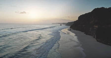 Sunrise at cliff silhouette of ocean bay coast aerial view. Summer nature scenery at sand beach with sun rise up. Nobody seascape at sunlight at sandy shore of Sumba island, Indonesia rocky shorelineの写真素材
