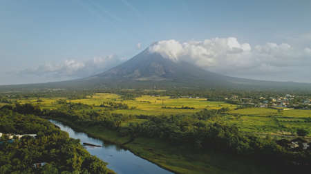 Hillside river at erupt volcano with green grass shore at Philippines countryside aerial. Fields, valley, meadows of nobody nature landscape. Cinematic scenic of Mayon mount erupt at mist hazeの写真素材
