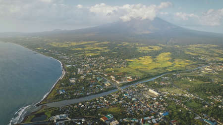 Mist at volcano eruption aerial. Clouds of haze over Mayon mount peak. Tropical farmland at lush green valley with plants and grasses. Nobody nature landscape of Philippines countryside with mountainの写真素材