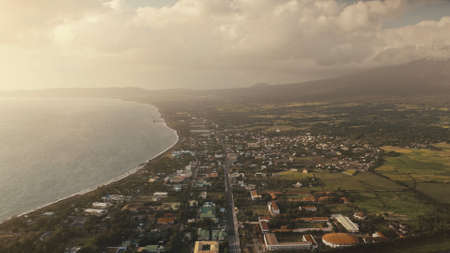 Aerial sun cityscape at ocean bay. Urban streets with houses at green valley. Tropic nature landscape at sea shore. Summer vacation scenic at sunny day with mist. Sun reflection at water surfaceの写真素材