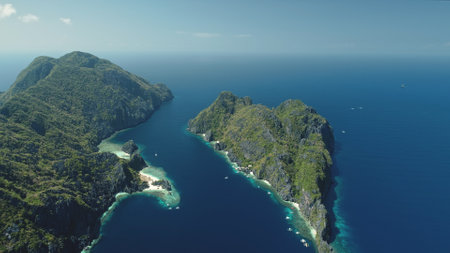 El Nido Islands at blue sea bay aerial view. Green mountain isles with tropical forest at sand beach. Wonderful seascape with greenery islets of Philippines Archipelago. Cinematic drone shotの写真素材