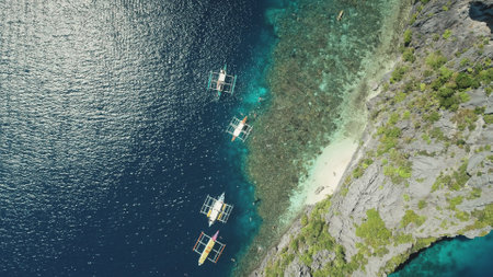 Top down of traditional boats at rock ocean coast aerial view. Majestic seascape with vessels at sun shine reflection on water surface. Summer cruise vacation at El Nido Island, Philippines, Asiaの写真素材