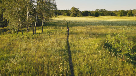 Slow motion woman riding bike at green grass meadow. Summer nature landscape at sunny day. Leafy forest at country road. Traveler girl on bicycle. Active sport. Rural vacation at Kyiv, Ukraine, Europeの写真素材