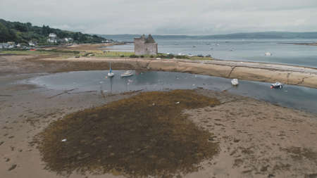Brown sand beach of sea bay aerial. Flying bird at ocean shore. Old historic castle ruins on seaside lake. Sea gulls at summer day. Seascape ships, yachts at Loch-Ranza, Arran Island, Scotland, Europeの写真素材