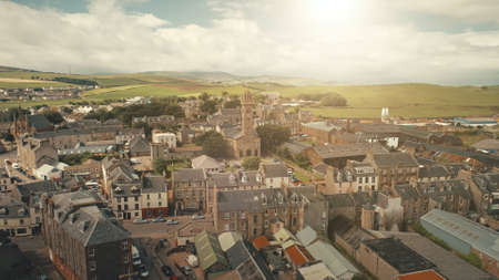 Sun cityscape at traffic road cars drives aerial. Historic buildings at streets of Campbeltown city, Scotland, Europe. Downtown houses and architecture landmark. Cinematic sunlight urban sceneryの写真素材