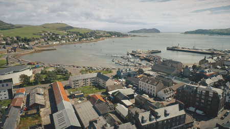 Harbor town cityscape aerial. Seascape with yachts, ships at urban street with road. Cars drive at traffic highway. Modern buildings at ocean shore of Campbeltown, Scotland, Europe rise-up drone shotの写真素材