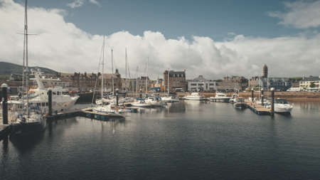 Ships, yachts at ocean bay aerial. Cityscape with modern and historic architecture landmark at port city of Campbeltown, Scotland, Europe. Downtown streets: old buildings at traffic highwayの写真素材