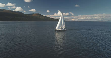 Sailboat sun reflection at seascape aerial. Racing yacht sail at open sea. Luxury ship at summer marine cruise at Arran Island, Scotland, Europe. Cinematic soft sun light over serene ocean bay waterの写真素材
