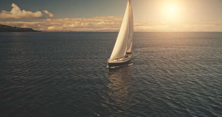 Luxury yacht race in open sea with sun reflections. Serene seascape with sailboat. Yachting at ocean bay water. Cinematic summer cruise at Arran Island, Scotland, Europe. Aerial panorama viewの写真素材