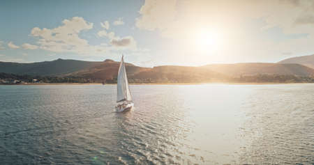 Sailing yacht in wind waves at Arran Island sea bay in Scotland. Amazing seascape at Brodick port city. Lonely sail boar race at sun shine with fluffy clouds. Serene water scape and transportationの写真素材