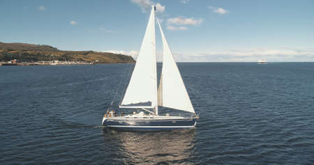 Luxury yacht at open sea racing under sails aerial. Amazing seascape of ocean bay with ship. Epic sail boat at Brodick pier harbor, Arran island, Scotland, Europe. Cinematic summer cruiseの写真素材