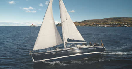 Closeup aerial of sailing yacht at sea bay. Sun seascape with sail boat. Luxury ship at open sea. Brodick harbor ocean bay with sailboat. Cinematic summer cruise at Arran island, Scotland, Europeの写真素材