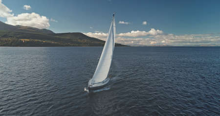 Closeup yacht race at ocean shore with green mountains. Seascape with luxury ship under white sails. Vessel cruise at open sea bay. Marine vacation at summer day. Nobody nature landscape of Scotlandの写真素材