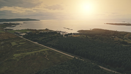 Green forest at sun sea shore. Nobody nature landscape. Farmland fields, pine forest at road with car. Whiskey distillery at ocean bay. Ellen Port, Islay Island, United Kingdom, Europeの写真素材