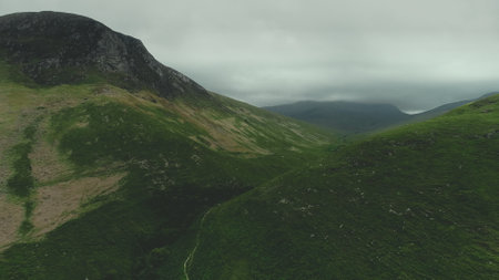 Scottish mountain ranges aerial view: path between green hills. Grey clouds wrapped top of mounts in summer day. Wild untouched nature scenery of island Arran. Footage Shot in 4K (UHD)の写真素材