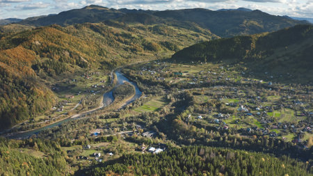 Mountain village at river aerial. Autumn nobody nature landscape. Countryside downtown at green grass valley. Cottages, houses at rural streets, roads. Settlement at Carpathian mounts, Ukraine, Europeの写真素材
