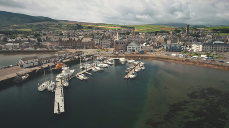 Sun dock with yachts aerial. Summer cityscape of port Campbeltown city, Scotland, Europe. Downtown streets with modern buildings. European urban scenery. Scottish seascape at sunlightの写真素材