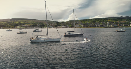 Aerial timelapse of sun sailing on luxury yachts, boats at calm sea bay. Sailboat regatta race. Amazing seascape at ocean coast of Arran Island, Scotland, United Kingdom. Cinematic summer cruiseの写真素材