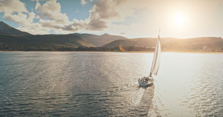 Sailing yacht in wind waves at Arran Island sea bay in Scotland. Amazing seascape at Brodick port city. Lonely sail boar race at sun shine with fluffy clouds. Serene water scape and transportationの写真素材