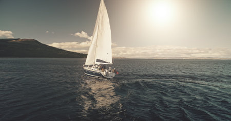 Aerial panorama of yacht race in open sea with sun reflections. Serene seascape with sailing boat. Luxury yachting at ocean bay water. Cinematic water transport scenery at summer cruise conceptの写真素材