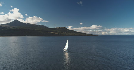 Aerial racing yacht at mountainous island. Luxury ship at mountain ocean coast. Sailboat regatta at sea bay. Sun reflect at Brodick pier, Arran isle, Scotland, Europe. Sail boat summer cruiseの写真素材