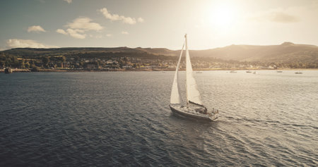 Aerial view of sun light on sail boat at ocean bay reflection. Highland sea coast with forest and mounts at bright sunlight. Nobody nature seascape at Brodick harbor with luxury yachts cinematic shotの写真素材