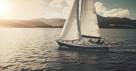 Aerial slow motion of yacht regatta sailing at sun reflection on ocean coast. Mountainous island of Arran shore with white sail boat. Nobody Scotland seascape of luxury lifestyle cinematic drone shotの写真素材