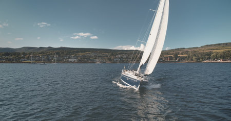 Racing yacht at sun ocean bay aerial. Nobody nature landscape of Arran Island. Brodick town cityscape at green highland. Cinematic Scotland seascape with water transport at drone shotの写真素材