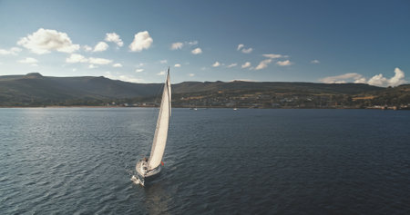 Yachting on ocean harbor aerial. Nature seascape at summer day. Regatta on luxury yacht. Sailboats cruise at open sea. Brodick port, Arran Island, Scotland. Cinematic drone shotの写真素材
