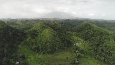Asia countryside aerial: green hill view at volcano smoke haze on horizon. Rural houses in Philippines majestic landscape with greenery hilly lands at Filipino island. Asian wild nature sceneryの写真素材