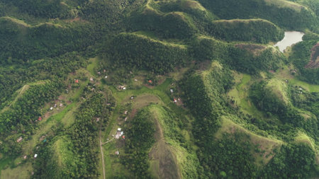 Rural green mountains ranges aerial view: greenery road and cottages at hilly countryside of Legazpi, Philippines. Small houses and way on hillside grass valley. Epic nature landscape. Soft light shotの写真素材