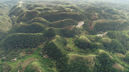 Green hill aerial: rural Philippines landscape of lake, building at hillside. Cinematic mist above mountains top of town Mayon, Asia. Scenic natural greenery of mounts ranges. Rise up drone shotの写真素材
