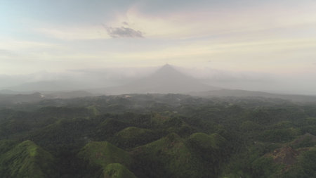 Jungle hills aerial at cloudy sky with Mayon Mount. Green plants at dusk summer day. Epic nature scenery of Legazpi city, Albay province, Philippines, Visayas archipelago, Asia. Cinematic drone shotの写真素材