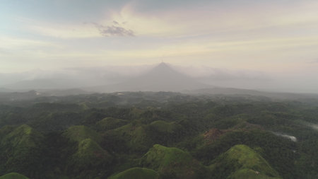 Countryside green hills at cloudy day. Mist Haze over mounts ranges at lush greenery. Nobody tropical nature landscape of Legazpi city, Philippines, Asia. Dramatic foggy rural scenery aerial shotの写真素材