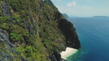 Majestic seascape of ocean bay greenery rocky shore at sand beach. Mountain island landscape with green tropic jungle forest. Boats at sea waterfront of Palawan Island, Philippines, Asia drone shotの写真素材