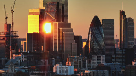 United Kingdom, London: London skyscrapers during a vibrant sunset. Warm sunlight reflecting in glass buildings, dynamic cityscape highlighting 30 St Mary Axe, the Gherkin. Aerial view droneの写真素材