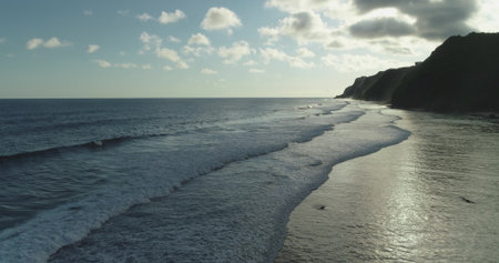 Gentle waves rolling towards the shore of Bali, Indonesia at sunset, creating a beautiful seascape with cliffs in the background, under a cloudy skyの写真素材