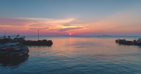 Tranquil seascape at sunset with colorful sky reflecting on the calm water of the Gulf of Thailand, with silhouettes of piers, boats, and cranes creating a peaceful and scenic viewの写真素材