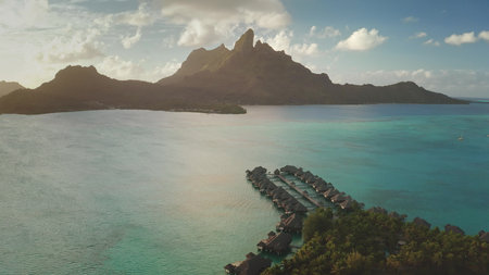 Golden hour casting warm light over mount Otemanu, highlighting turquoise waters surrounding luxurious overwater bungalows in pristine Bora Bora landscape of French Polynesiaの写真素材