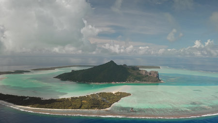 Maupiti island in French Polynesia presents breathtaking aerial view, vibrant turquoise waters, lush green vegetation, and dramatic mountainous landscape under a cloudy sky. Remote wild nature travelの写真素材