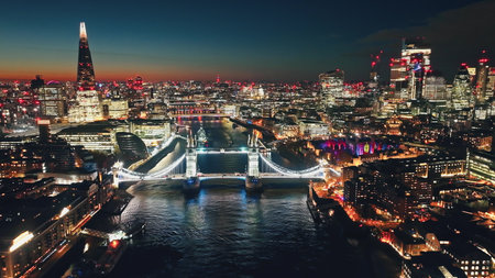 UK, London: Aerial view of famous Tower Bridge at night, The Shard and other landmarks along the Thames River, creating a stunning urban cityscape in colorful evening lights. Drone flight panoramaの写真素材