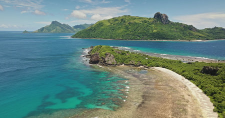 Fiji, Kuata island: Breathtaking aerial view of crystal clear turquoise water lagoon, vibrant coral reefs, wild sand beach, and lush vegetation. Green mountains under blue sky. Drone flightの写真素材
