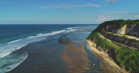 Stunning aerial drone revealing the mesmerizing beauty of Balangan Beach in Bali, Indonesia, with rhythmic waves, vibrant coral reefs, and lush green cliffsの写真素材