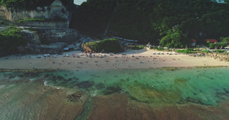 Aerial drone view of a beautiful beach in Bali, Indonesia, showing tourists relaxing on the sand, swimming in the crystal-clear turquoise water, and enjoying the stunning coastal sceneryの写真素材