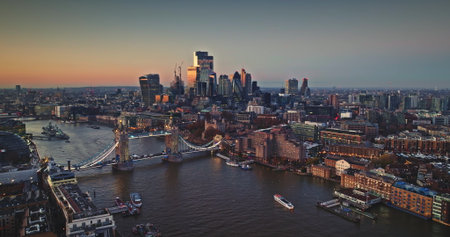 UK, London cityscape at sunset, iconic Tower Bridge spanning the River Thames, modern skyscrapers reflecting golden light against the twilight sky. Travel destination. Aerial drone flight panoramaの写真素材